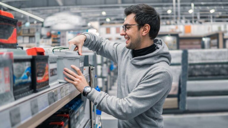 A male customer in an auto shop purchasing a car battery from a shelf.
