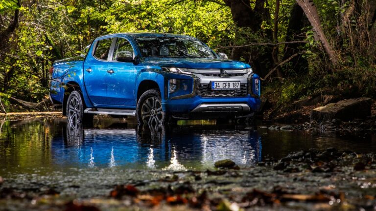 Front-side view of a bright blue and black Mitsubishi L200 on a small pool of water in front of greenery.