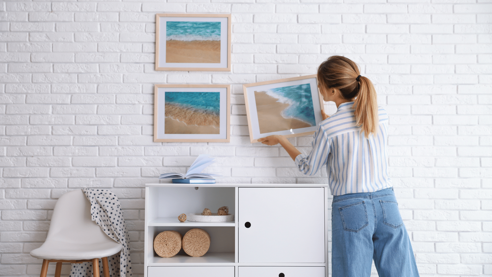 Decorator hanging picture on white brick wall in room. Interior design.