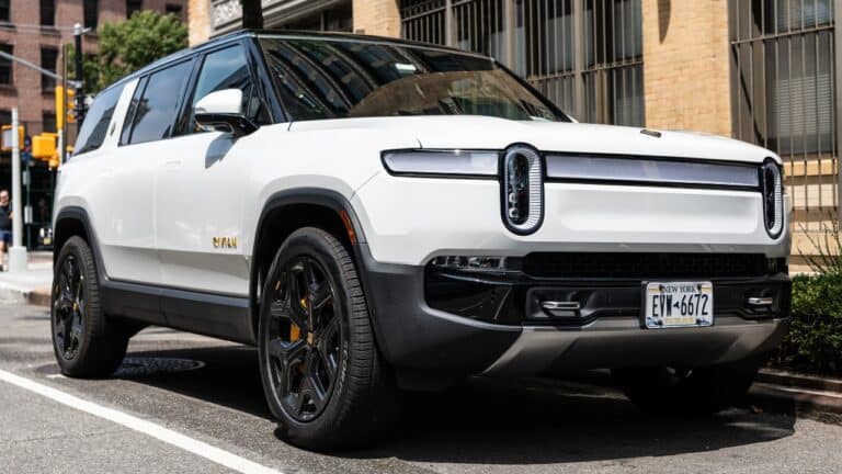 Rivian R1S SUV electric white car view from the front and passenger side, parked on the streets of New York. Front-side view, white car with black trim and accessories.