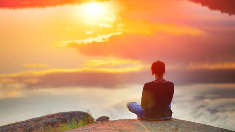relience woman sitting on cliff of mountain overlooking waterfall.