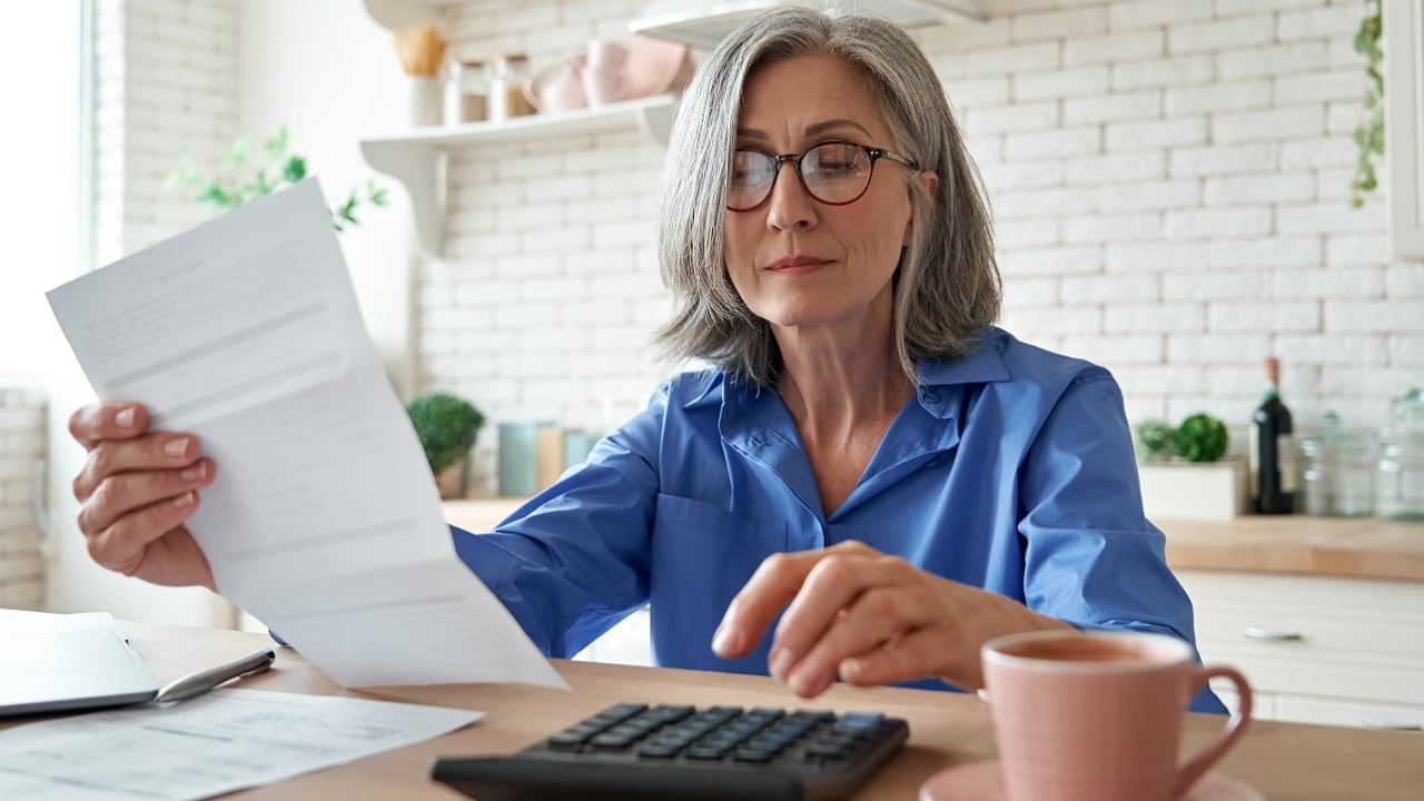 Senior mature business woman holding paper bill using calculator, older lady managing account finance, calculating money budget tax, planning banking loan debt pension payment sit at home kitchen table, Debt Management