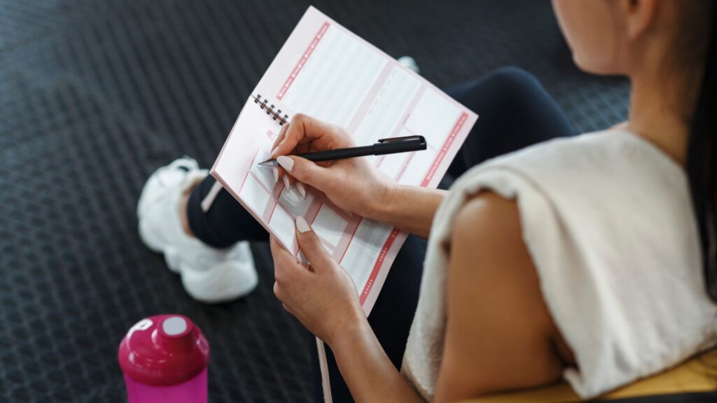 Workout planning. Young woman making her workout schedule in notebook indoors, above view.