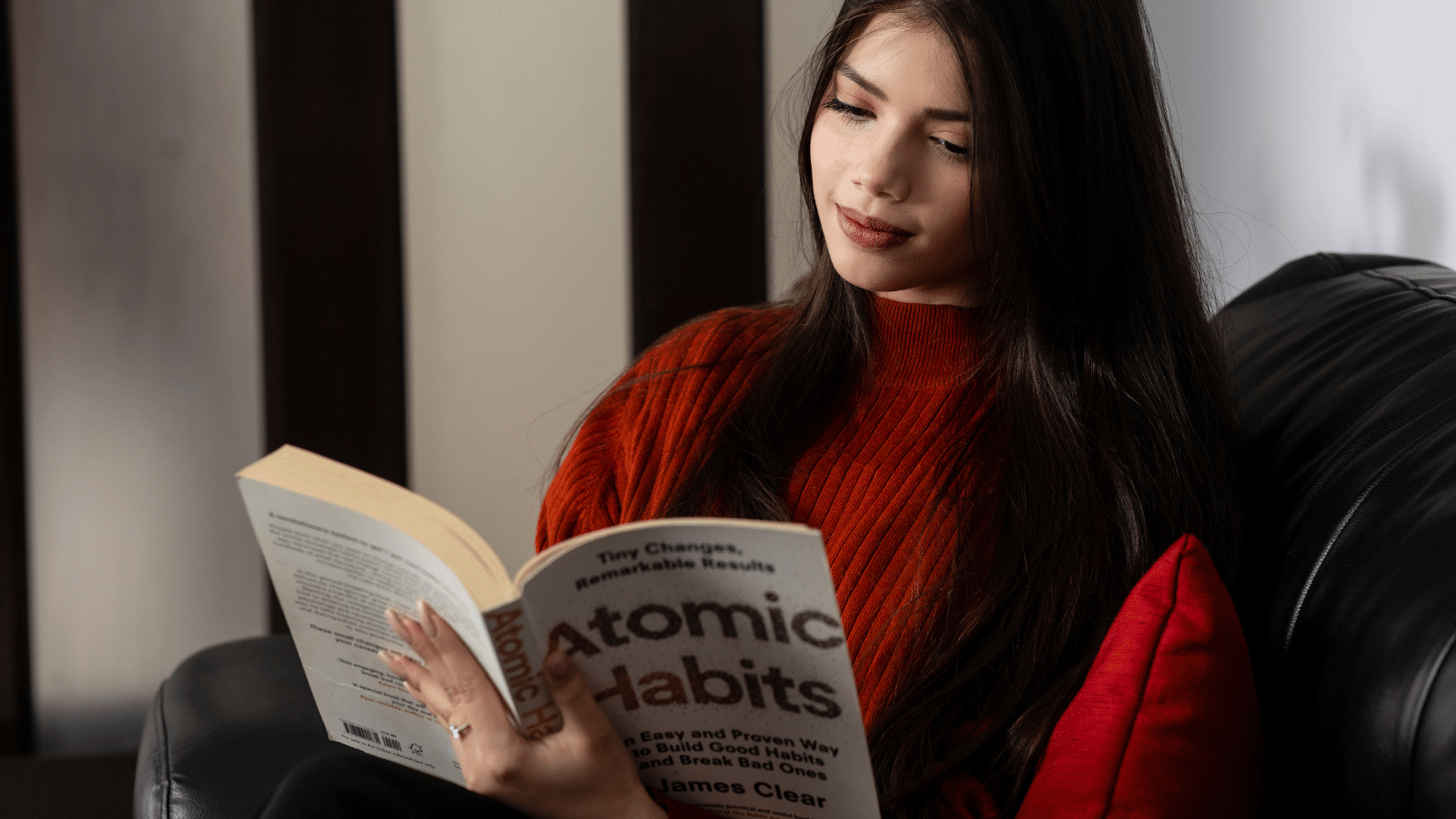A woman reads the popular book Atomic Habits by James Clear while sitting in her couch at home.