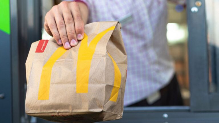 McDonalds worker holding bag of fast food. Hand with a paper bag through the window of mcdonalds car drive thru service.