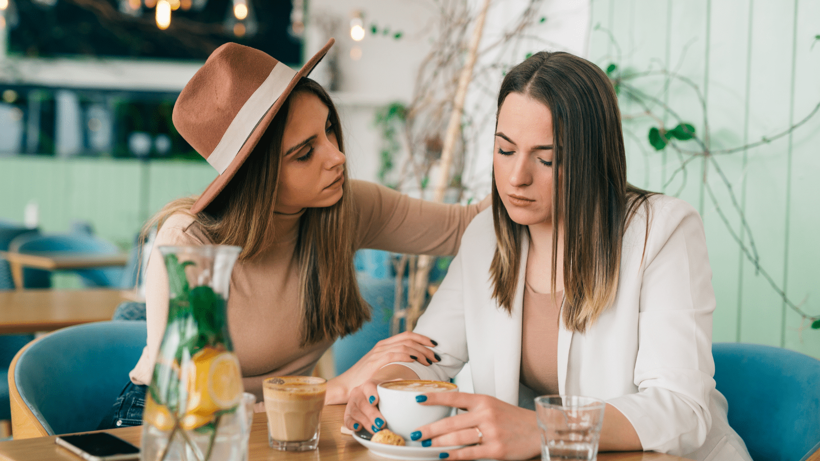 Woman comforts her friend in cafe during coffee break.