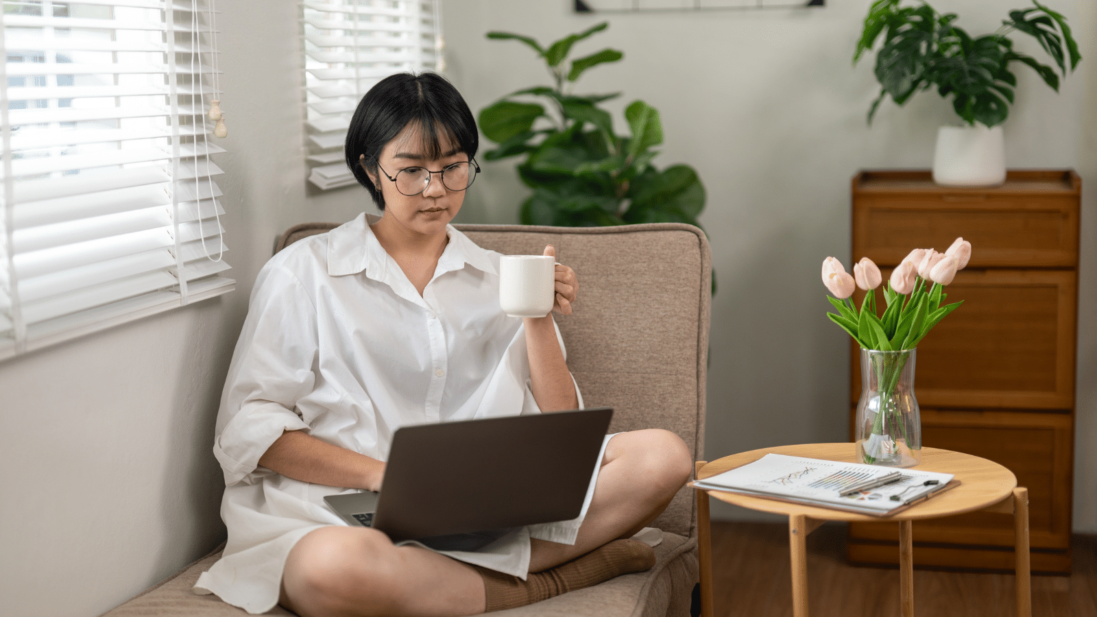 An adult woman sips her coffee while engaging with a laptop in a bright home office, reflecting a moment of tranquility amidst a busy workday.