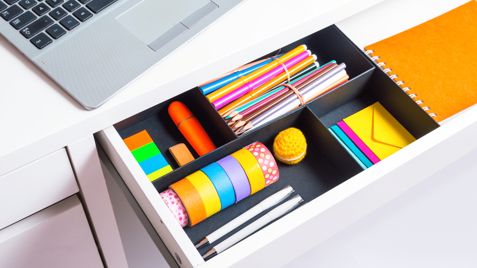 Opened office desk drawer with stationary and office supplies.