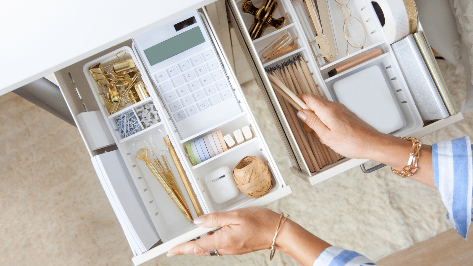 White work desk with organized stylish gold stationery is arranged very neatly in the drawers of the desk.