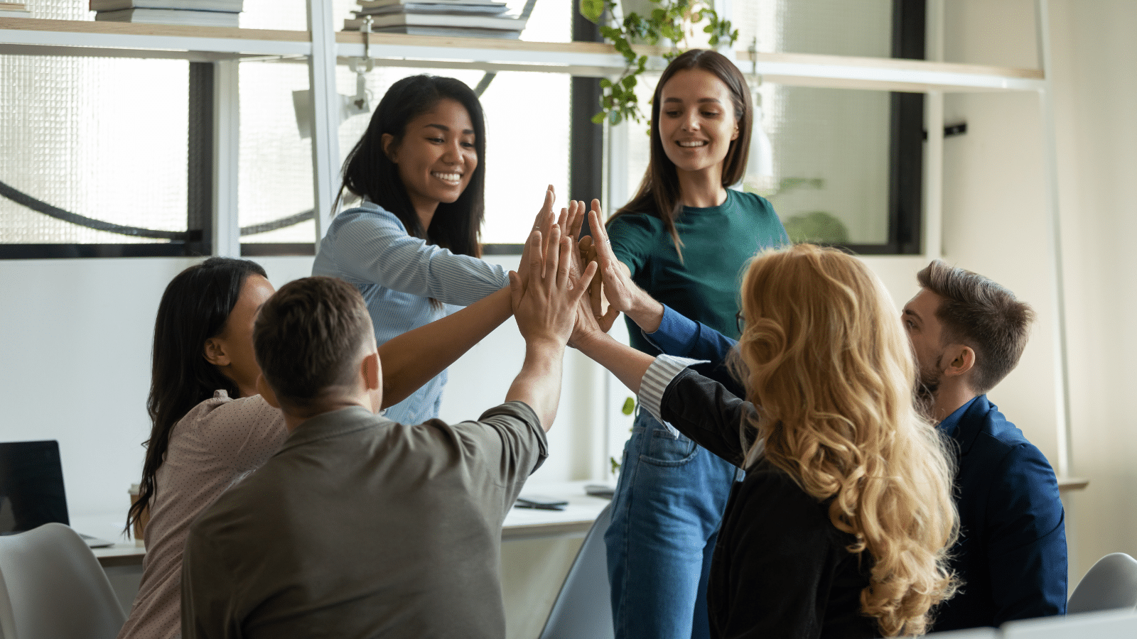 Successful diverse team giving high five, sitting in circle on meeting, discussing business project success.