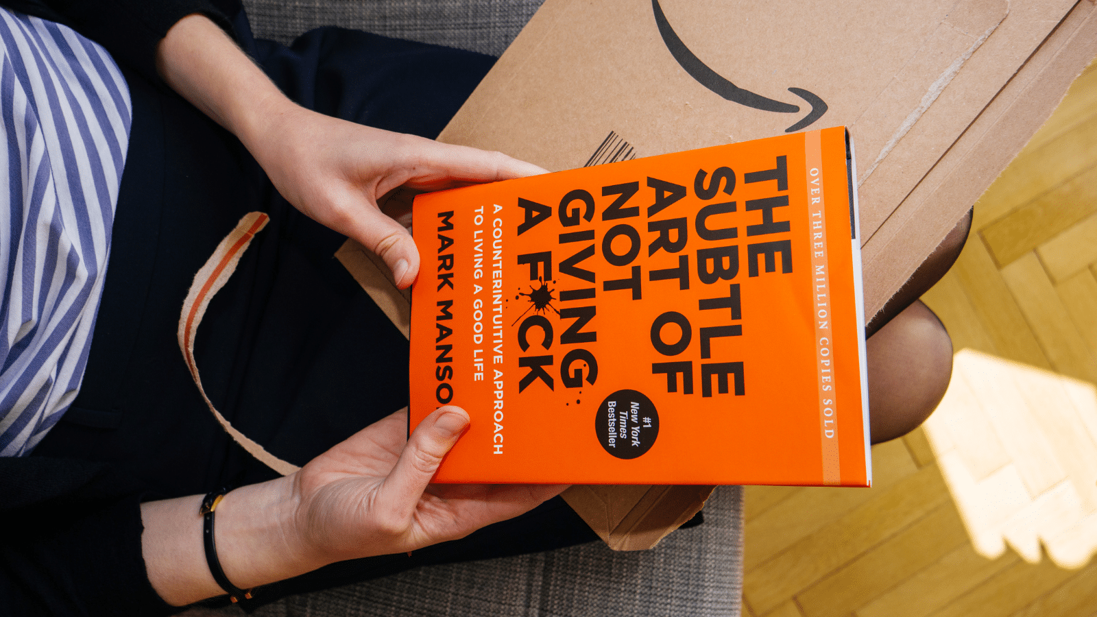 A woman holding the book "The Subtle art of Not Giving a F*uck" in her hands after opening her amazon package.