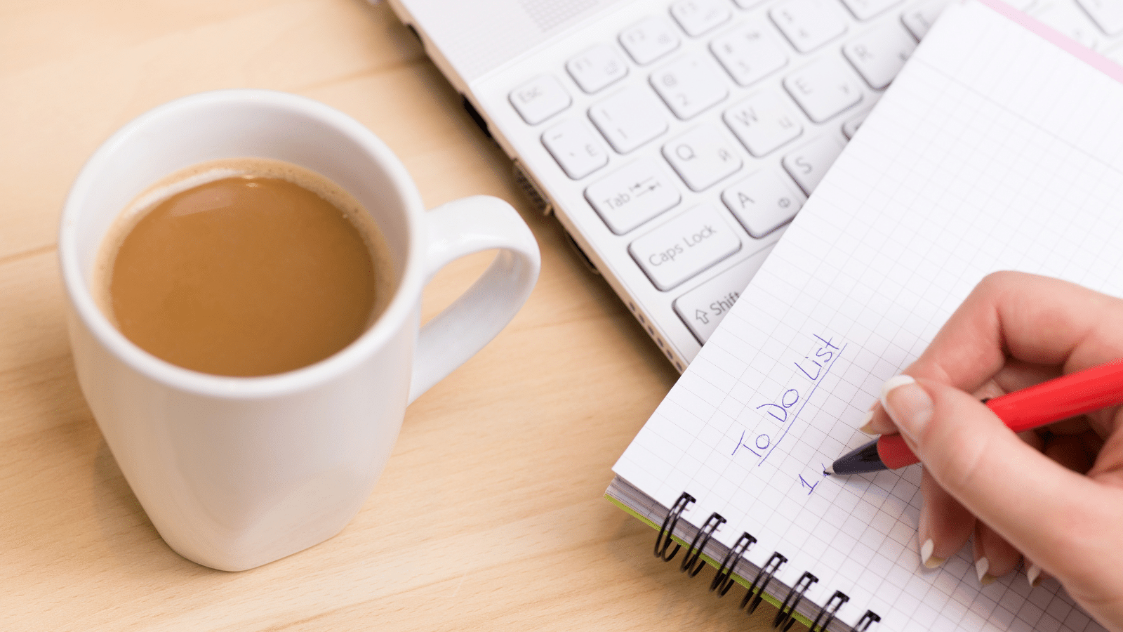 Woman writing and checking things off a 'to do list' at her desk with a cup of fresh coffee.