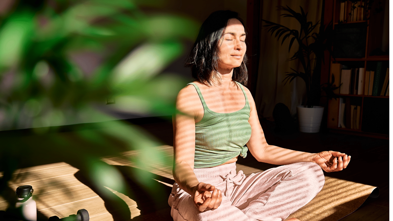 Woman practicing yoga and meditation at home sitting in lotus pose on yoga mat.