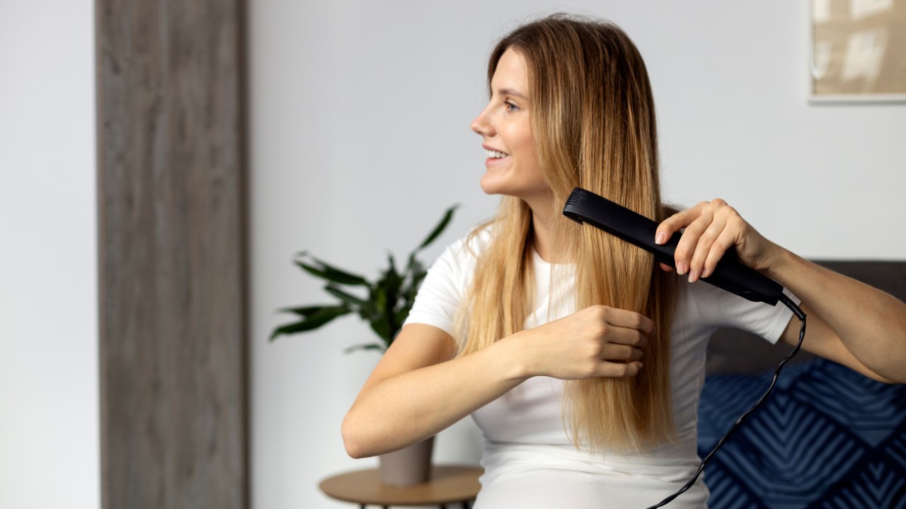 Young,Beautiful,Pregnant,Woman,Using,Hair,Straightener,And,Smiling,While