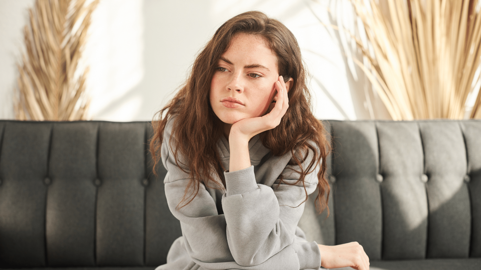 Woman sitting on couch looking confused and deep in thought with head in hand.