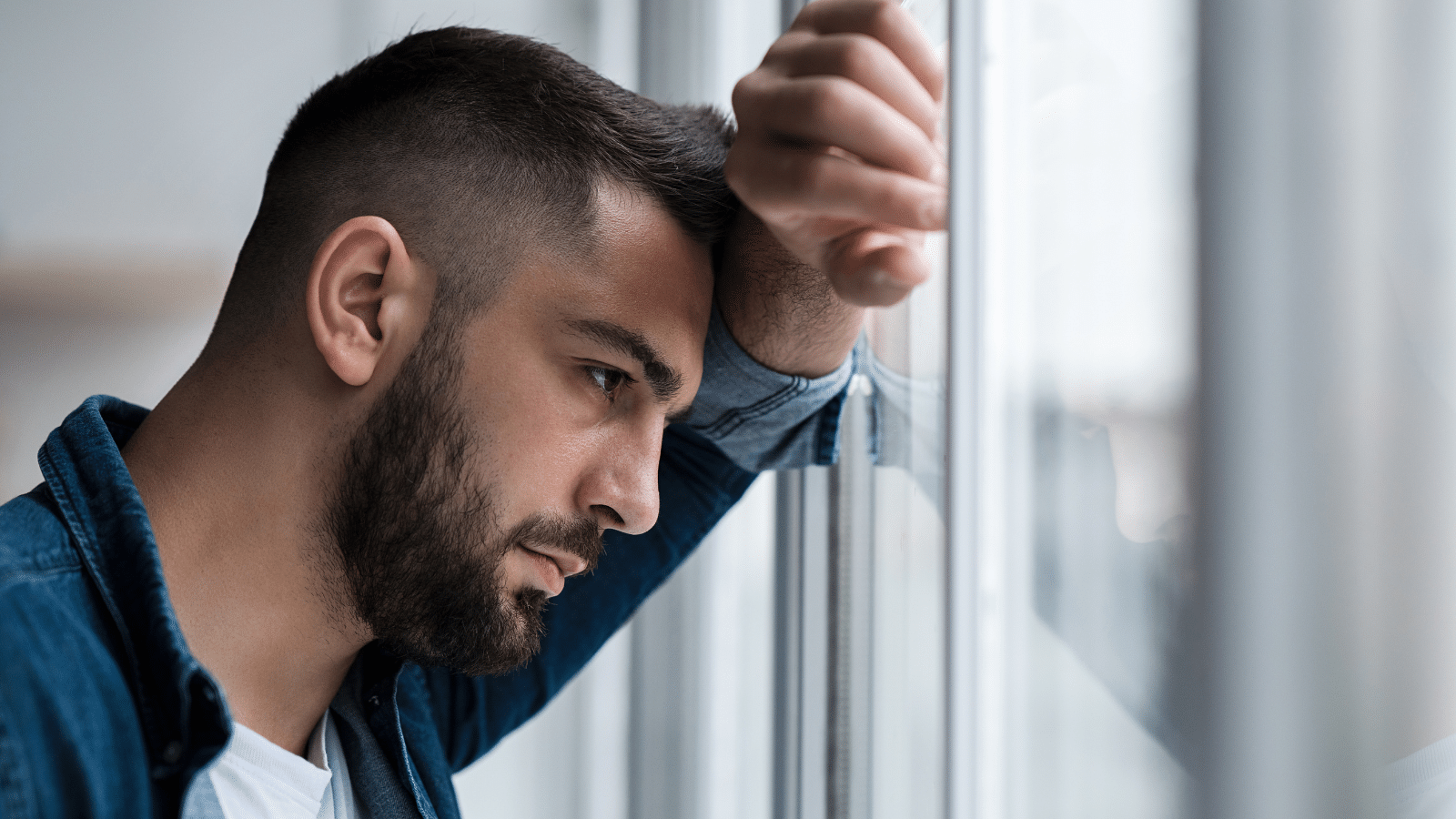 Depressed man deep in thought, feeling bad, looking outside window.