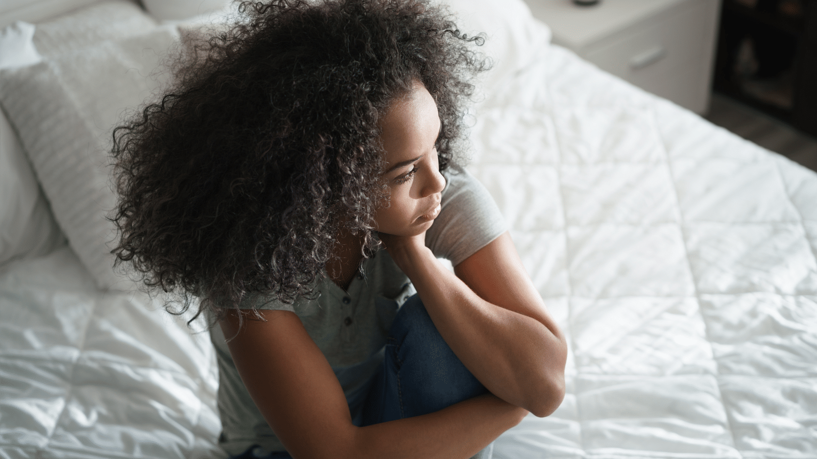 Young woman sitting on bed deep in thought or depressed looking at window.
