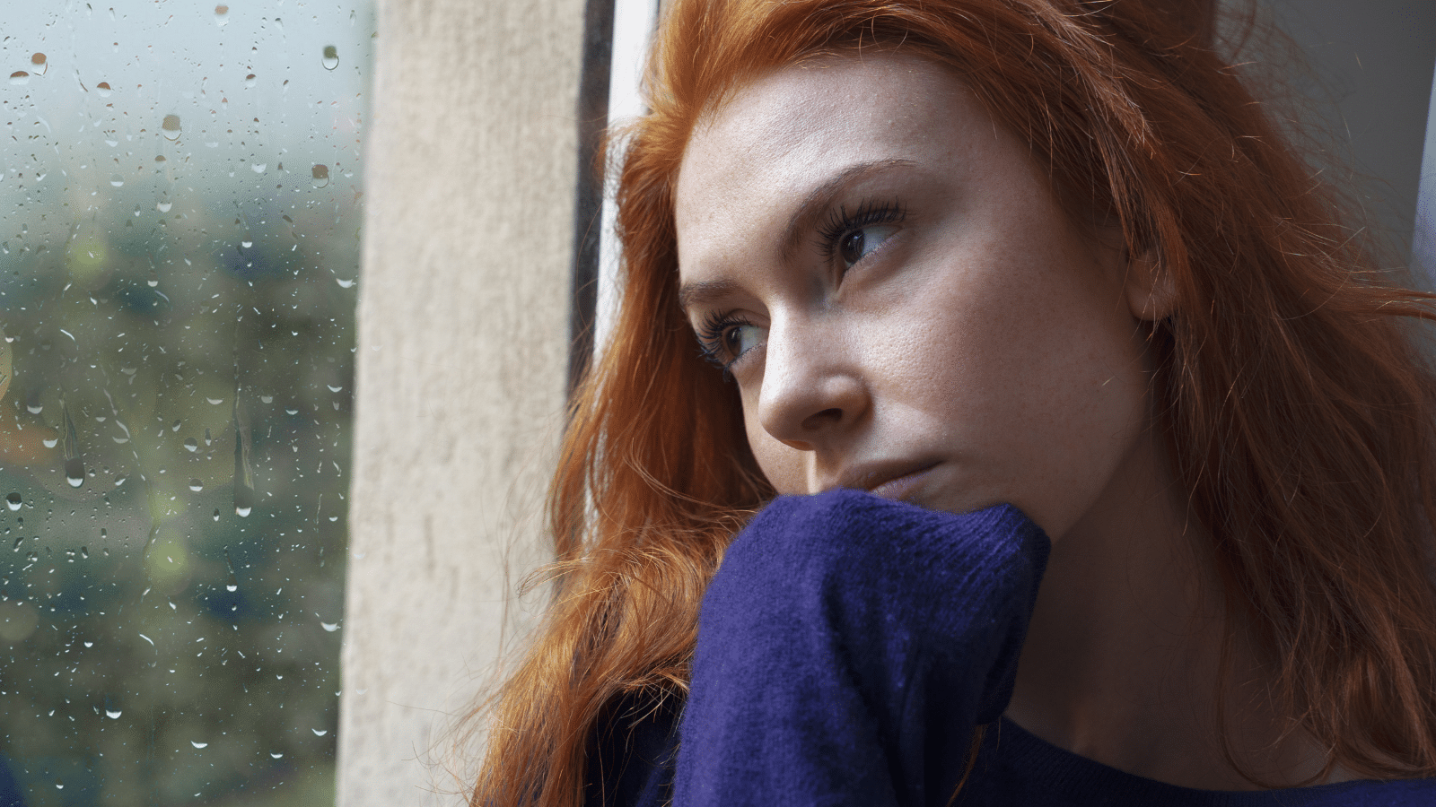 Portrait of worried girl looking through the window at home.
