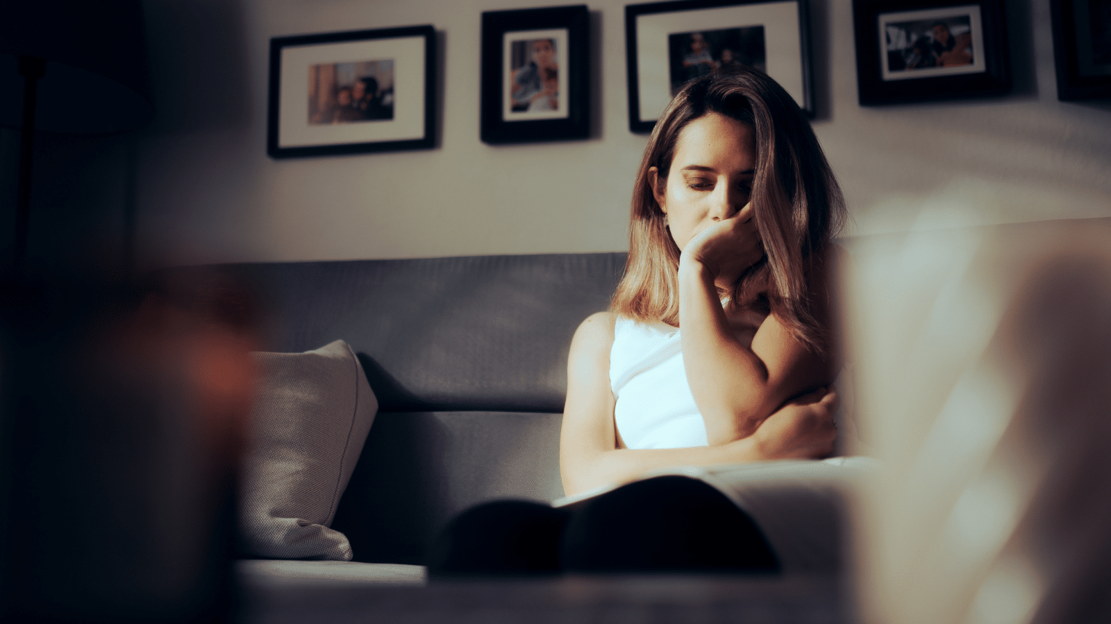 Sad depressed woman alone at home sitting on a sofa feeling anxious.
