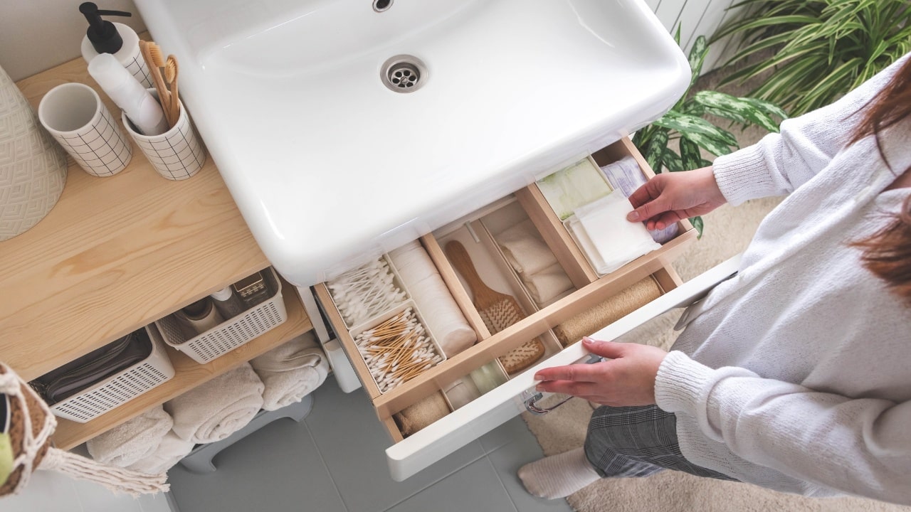 Top view of woman hands neatly organizing bathroom amenities and toiletries in drawer or cupboard in bathroom.