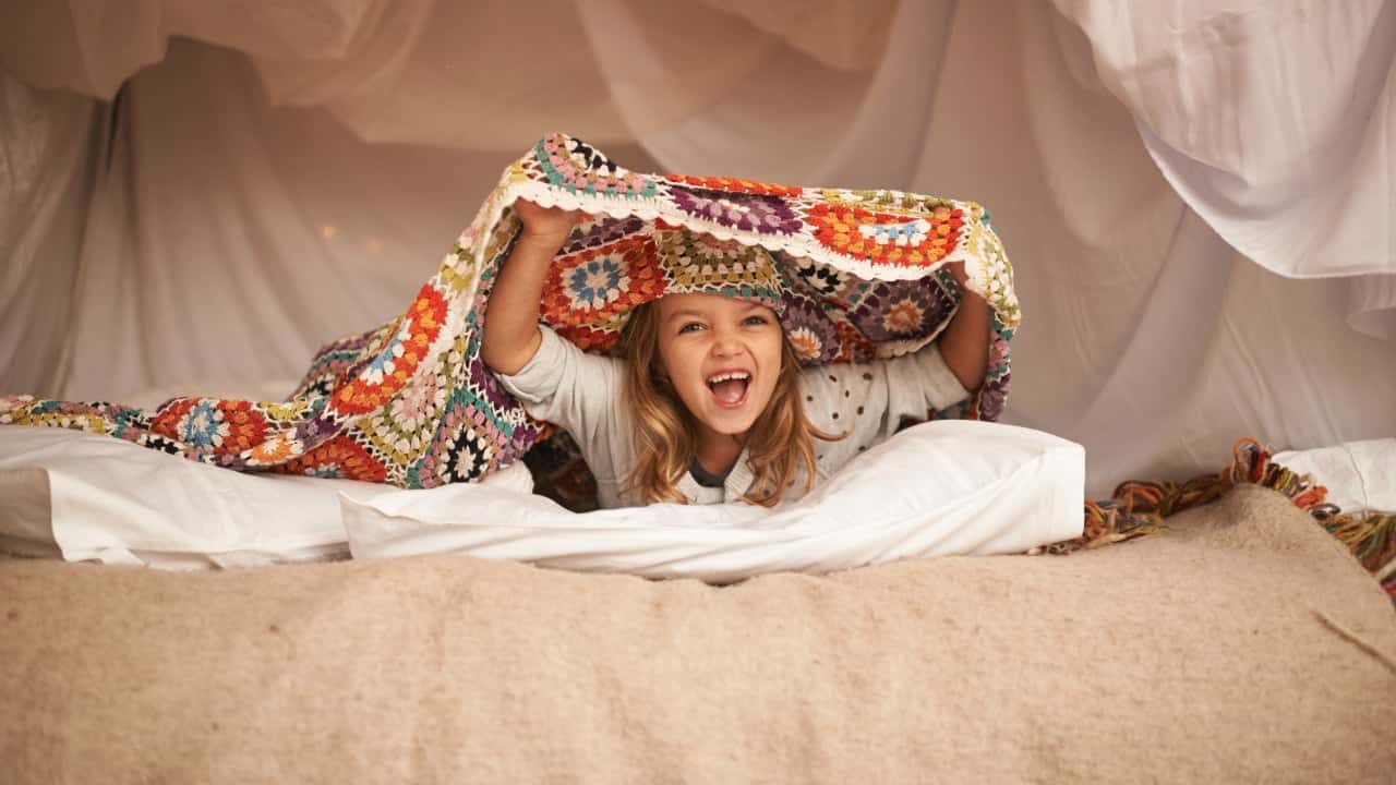 A little girl hides in a blanket fort, under a crocheted blanket, and roars.