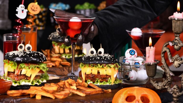 A witch's hand takes a Witch cocktail with eyeballs in a martini glass from the Halloween party table.