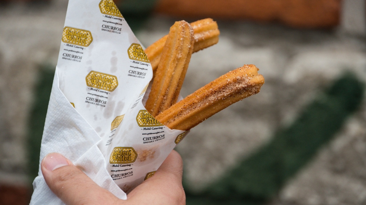 A hand holding churros with cinnamon sugar in a paper cone.