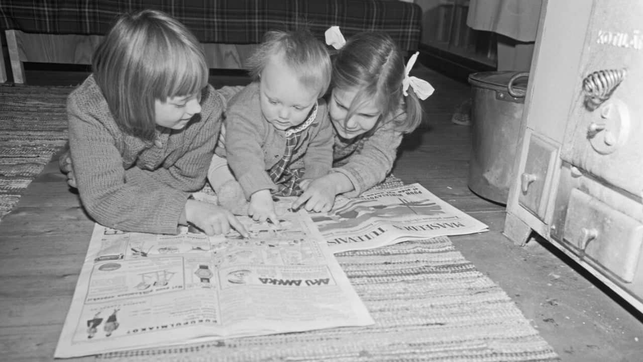 Three children reading a newspaper together on the floor.
