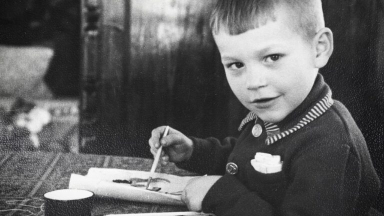 A vintage photo of a boy painting and looking at the camera