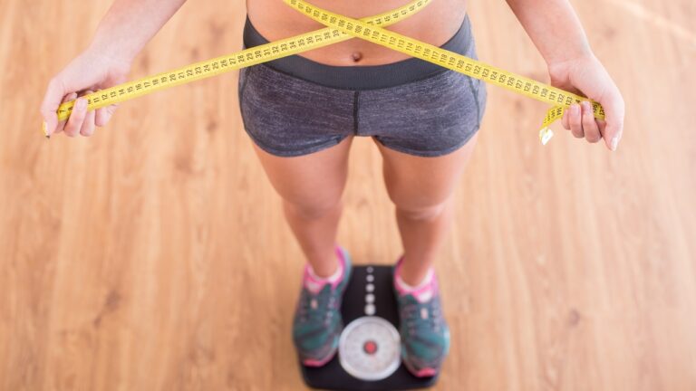 Top view of pretty slim woman with measure around her body is standing on the scales.