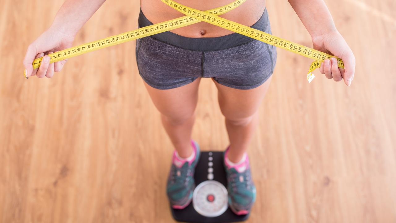 Top view of pretty slim woman with measure around her body is standing on the scales.
