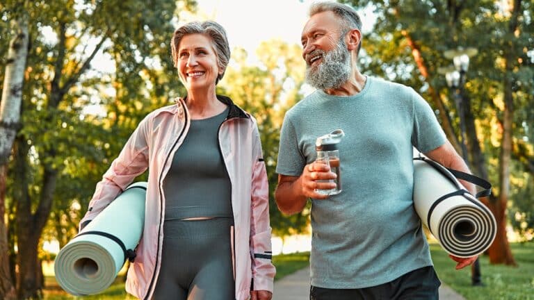 Active life of older people. Happy sports couple going for a workout outdoors, holding exercise mats and water. Health and recovery, healthy living, hobbies in retirement
