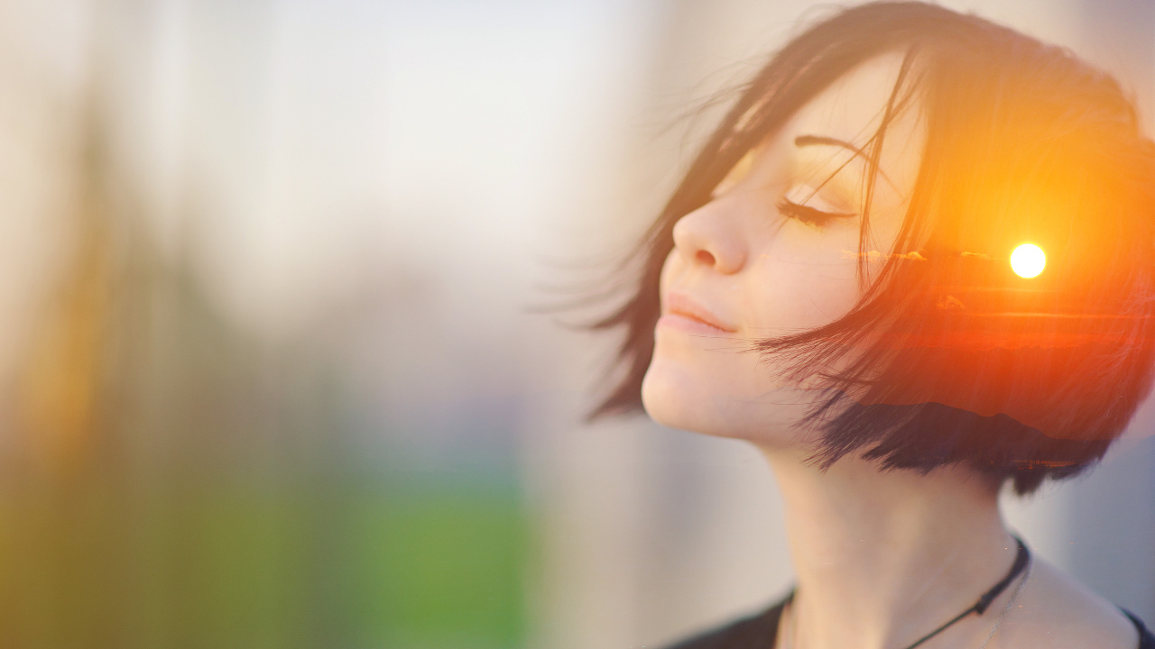 A double-exposed photo of a young woman closing her eyes and raising her head, while an image of the shining sun is projected onto her head, as if she is thinking positive thoughts