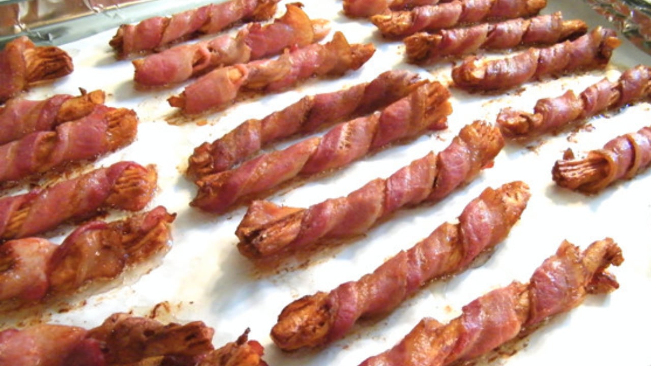Bacon-wrapped breadsticks baking on a sheet pan