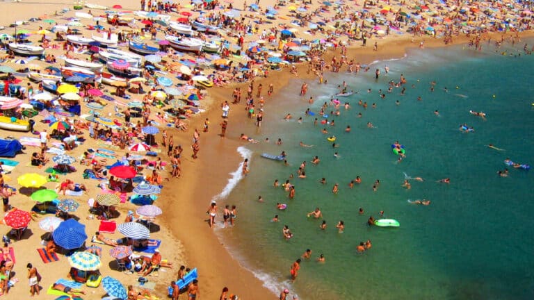 Aerial view of crowded beach peppered with sunbathing tourists and open umbrellas.
