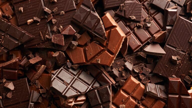 A variety of different delicious-looking chocolate bars and candy bars, broken and in a pile.