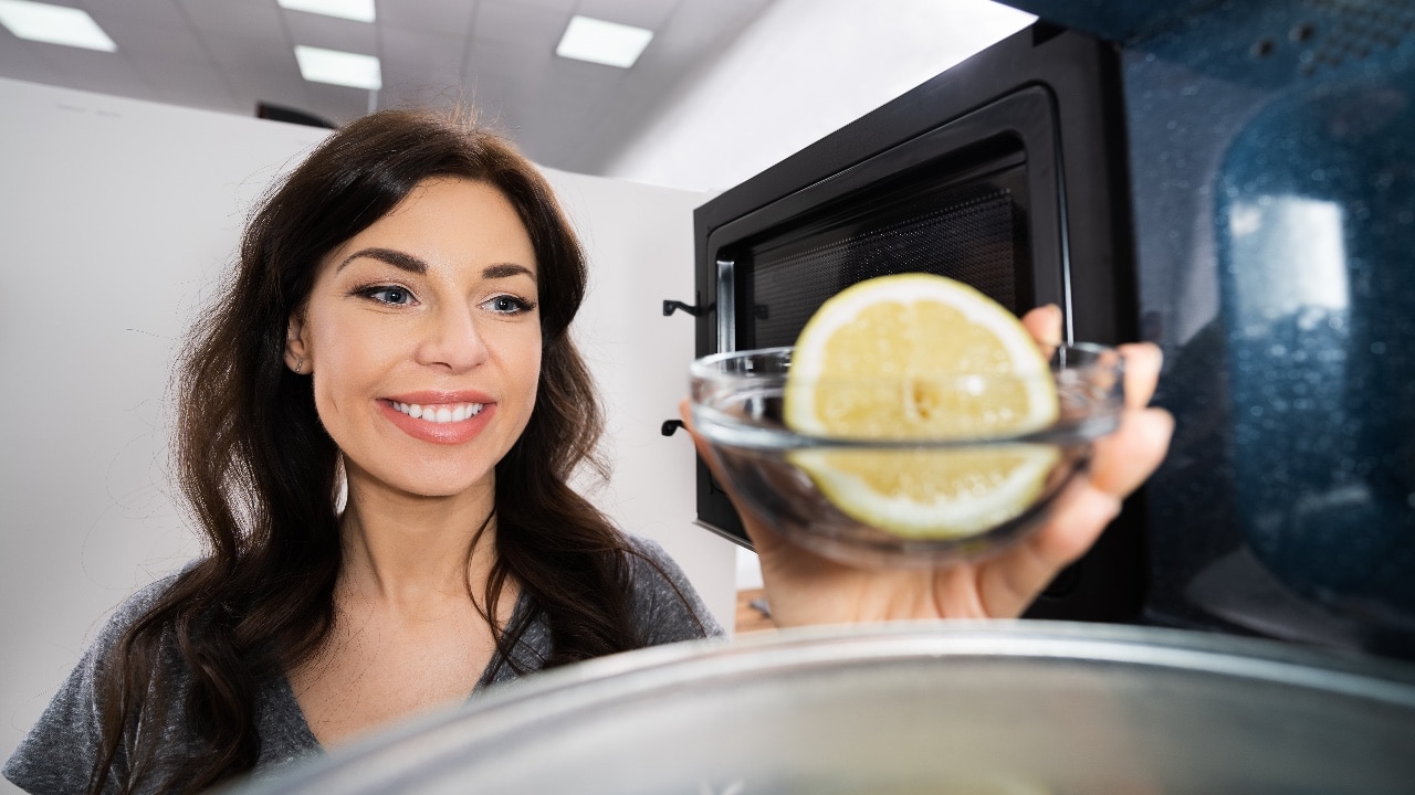 Woman putting a bowl of water and lemon in microwave to clean it