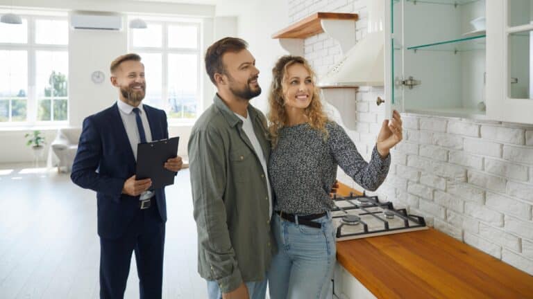 A male realtor leads a young couple through a new home tour.