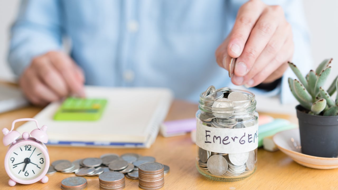 man hand is putting a coin in a glass bottle on wooden table, Investment business, retirement, finance , tax , emergency fund and saving money for future concept.