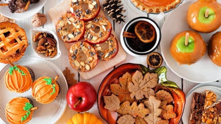 Autumn desserts table scene with various sweet fall treats. Top view over a white wood background.