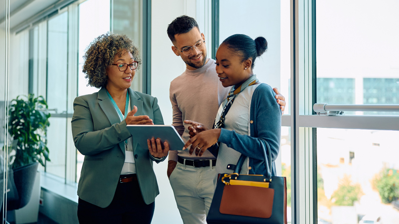 An older woman, a young man, and a young woman look at information on a tablet, receiving good news