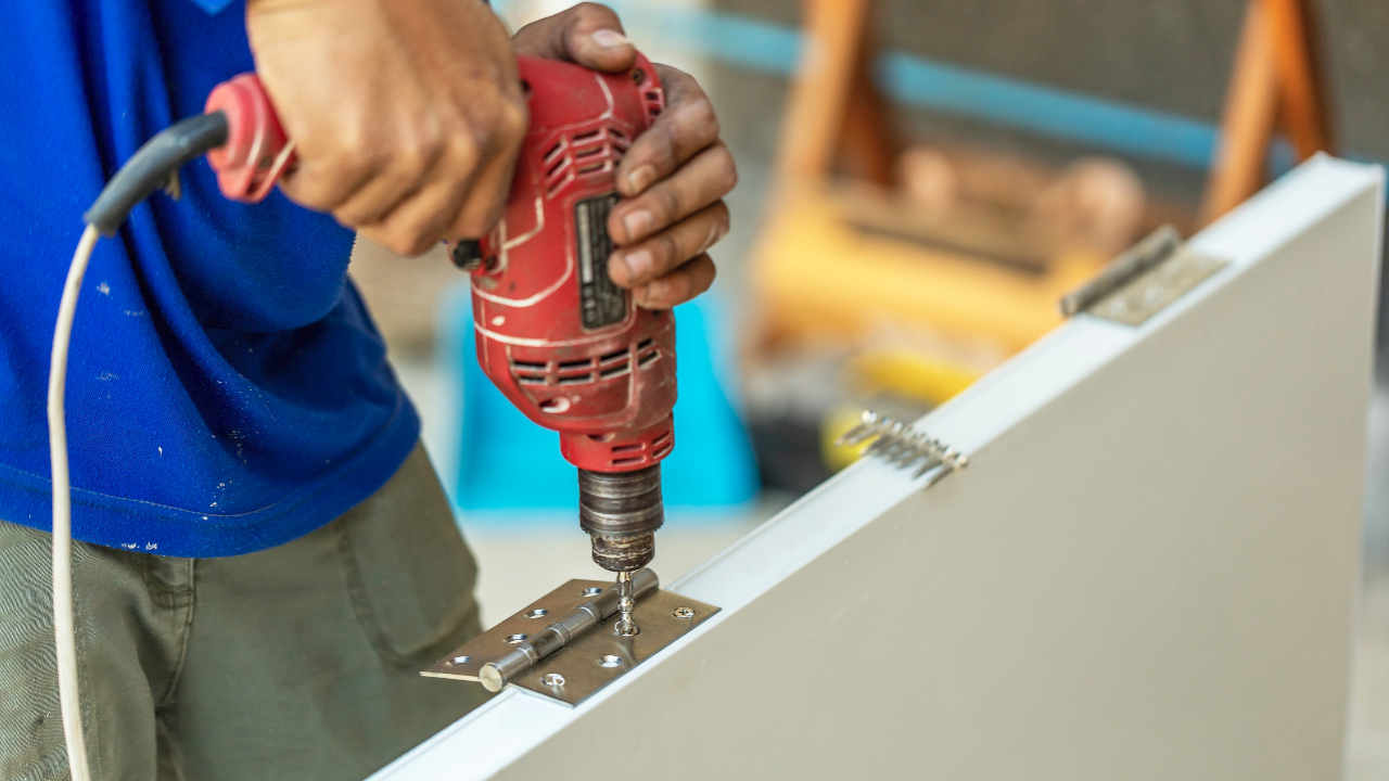 Using a power drill to sink screws into a new door hinge