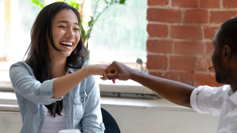 Two young professionals share a fist bump and laugh