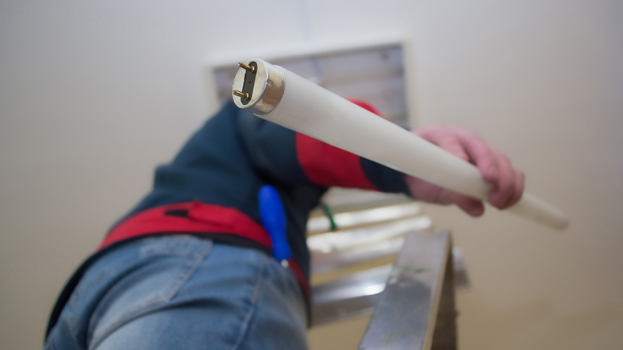 Person on ladder installing ceiling fluorescent lamp tube