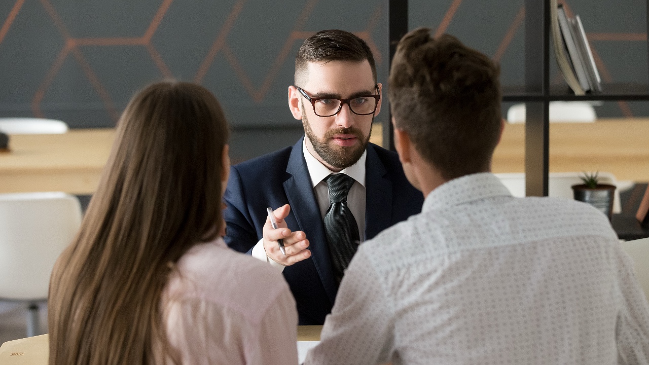 financial advisor or bank worker in suit and glasses consulting young couple