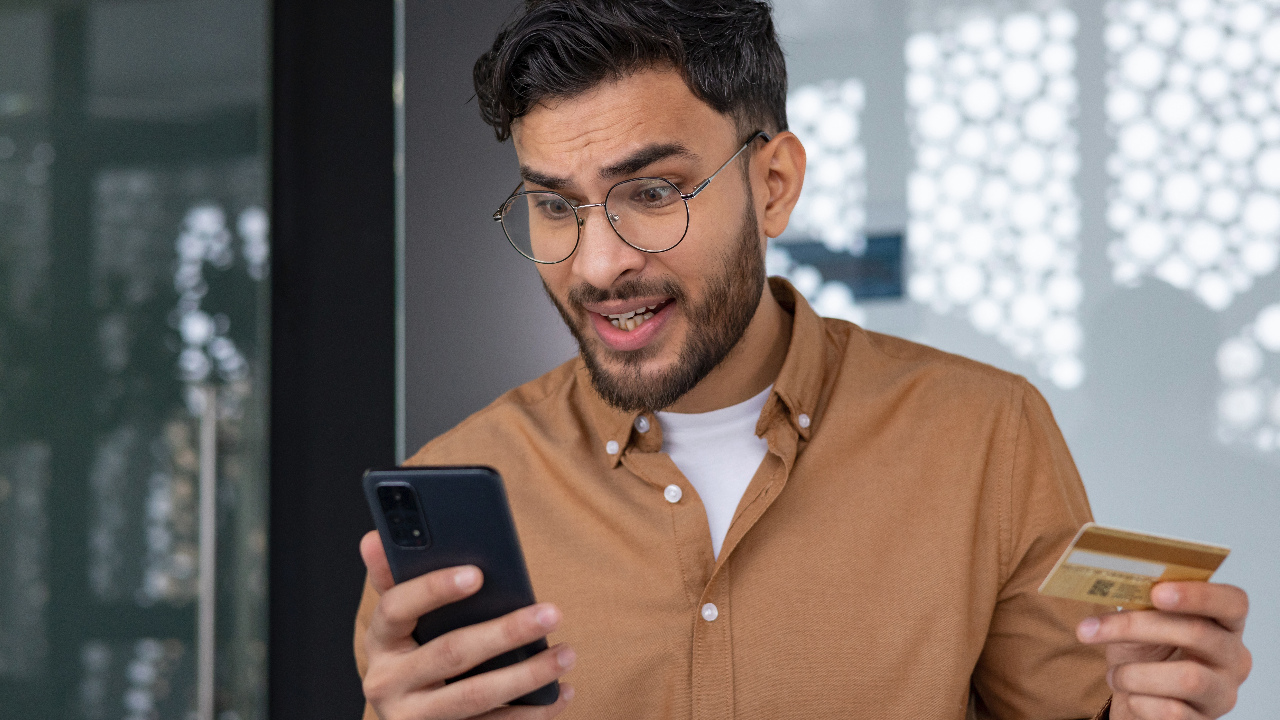 Man looks alarmed with credit card and phone in hand