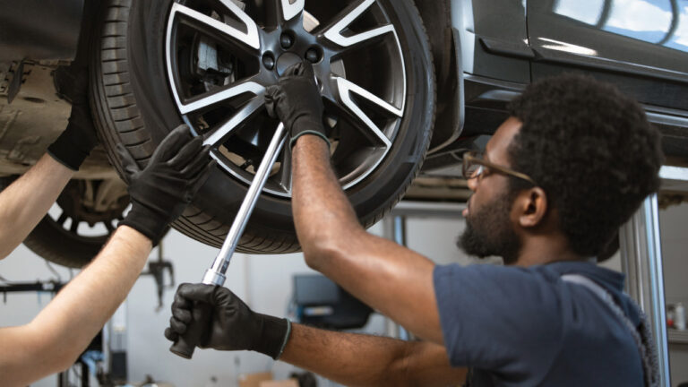 A mechanic with extended wrench works on lug nuts of a tire of a car on lift