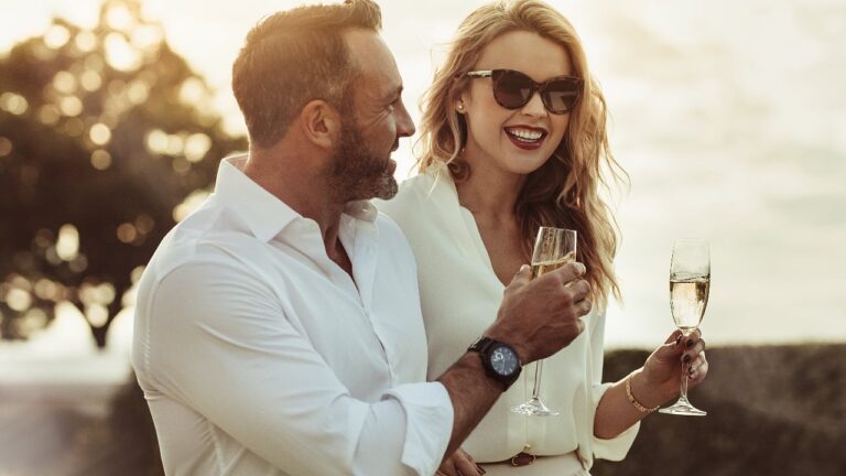 Smiling man and woman enjoying a glass of wine outdoors.