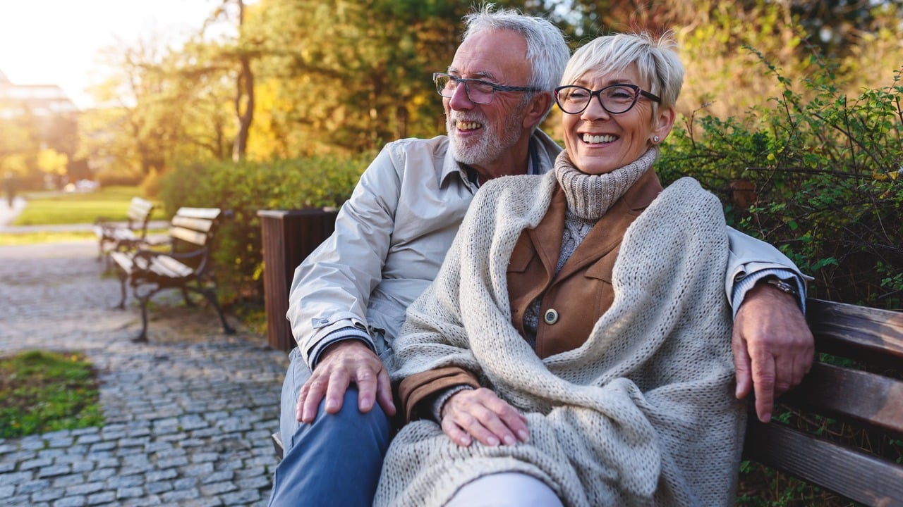 Smiling senior couple sitting on the bench in the park together enjoying retirement.