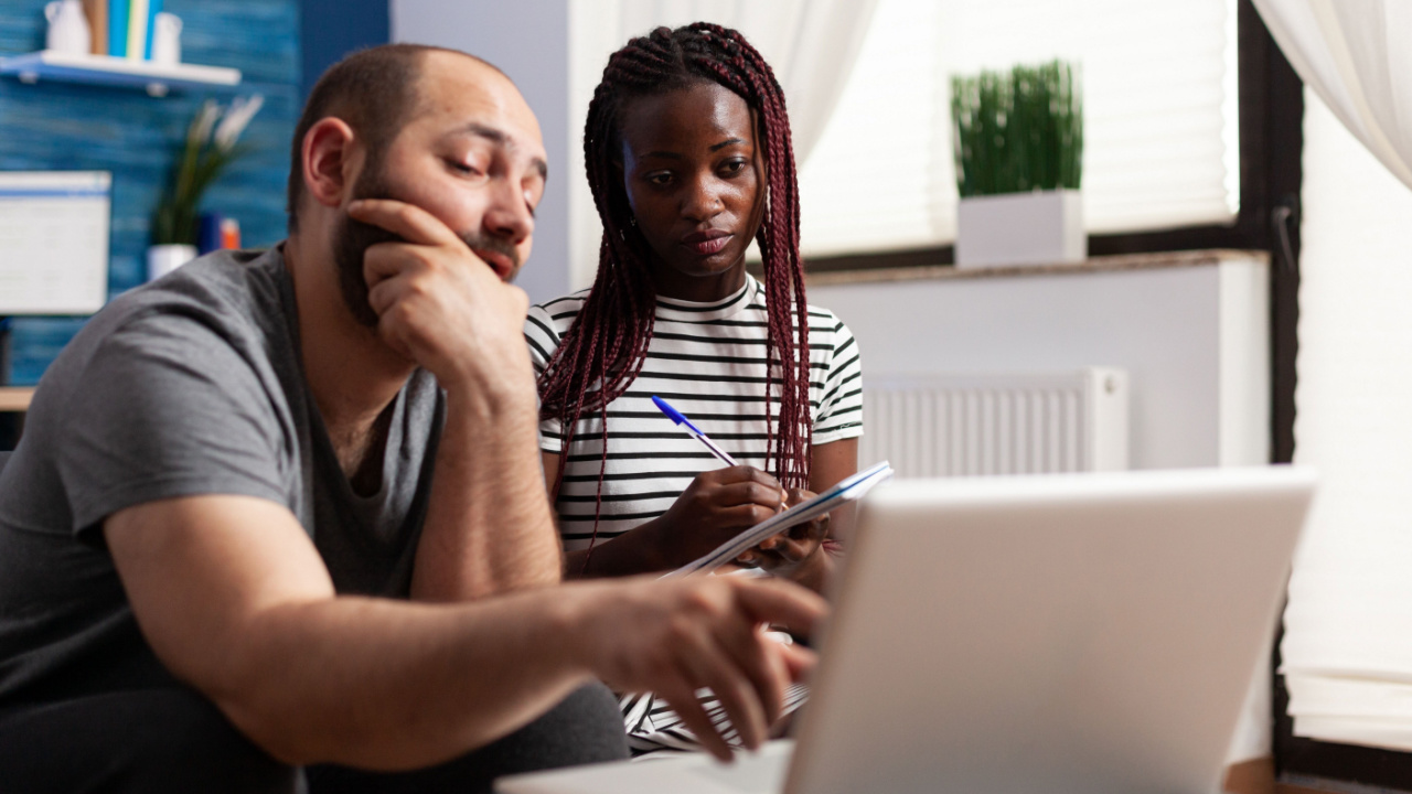 Worried couple looking at laptop screen while pointing out financial errors.